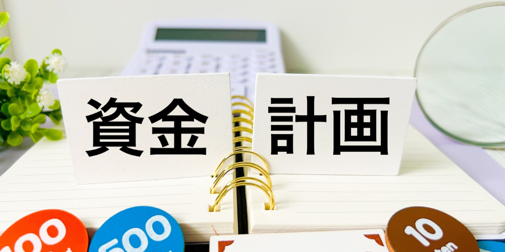 ノートの上に ‘資金’ と ‘計画’ の文字が書かれた白いブロックが並び、背景に電卓と硬貨が配された構図
