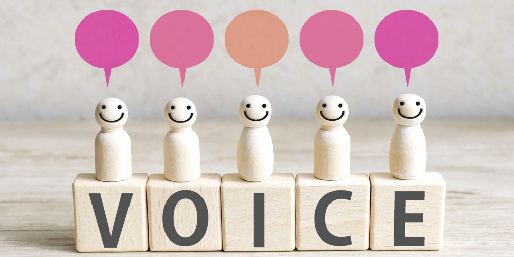 木製の人形が5体並び、それぞれ上にピンクやオレンジの吹き出しアイコン、足元のブロックで ‘VOICE’ と綴られているイメージ