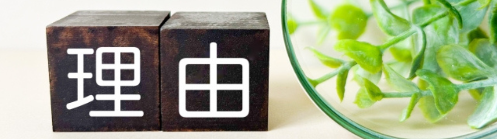黒い木製ブロックに書かれた「理由」の文字とガラス容器に入った植物