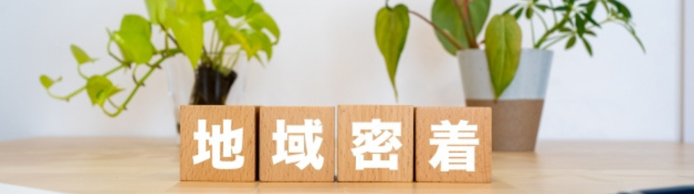 観葉植物と木製ブロックに書かれた「地域密着」の文字。地域とのつながりを大切にする姿勢を表す。