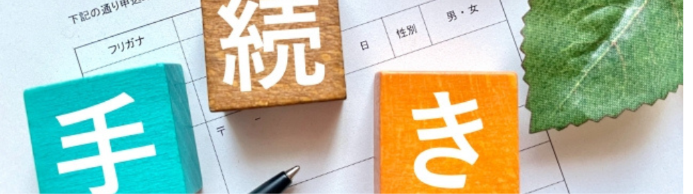 申請書の上に置かれた「手続き」を示すカラフルなブロックと葉。住まいや制度に関する手続きをイメージ。