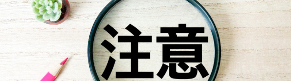 虫眼鏡で強調された「注意」の文字とピンクのペン、観葉植物の装飾