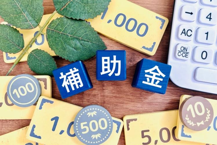 「補助金」の文字が書かれた青いブロックと電卓、木製コインや葉が並ぶ住宅支援金のイメージ