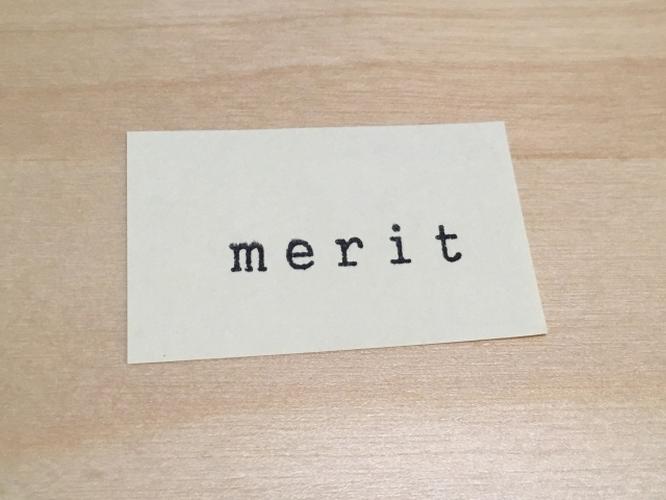 木目調のテーブルの上に置かれた「merit」と印字されたカード、利点やメリットを示すイメージ