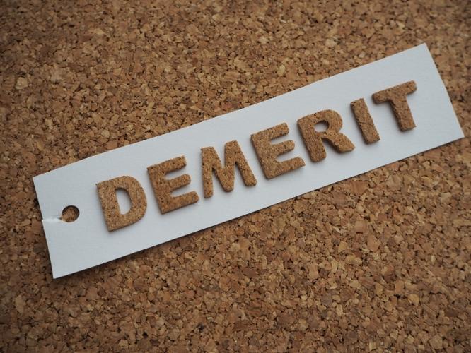 コルクボードの上に置かれた「DEMERIT」の文字が書かれたラベル、欠点や注意点を表すイメージ