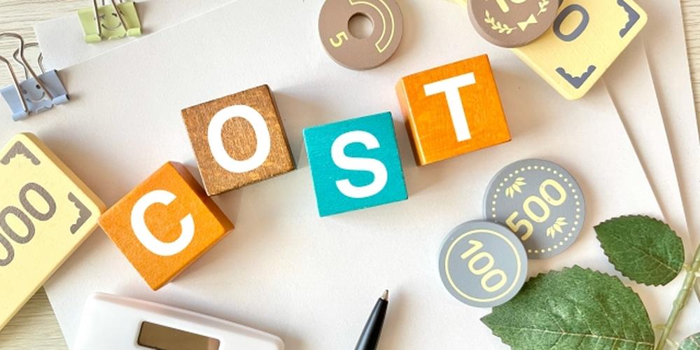 「COST」と書かれたカラフルなブロックと、電卓・コイン・紙幣風のパーツが並ぶコスト計算のイメージ。