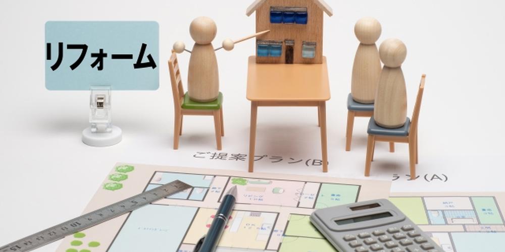 住宅のリフォームプランを検討する家族のイメージ図。間取り図や電卓、模型の家と木製の人形で会議の様子を表現。