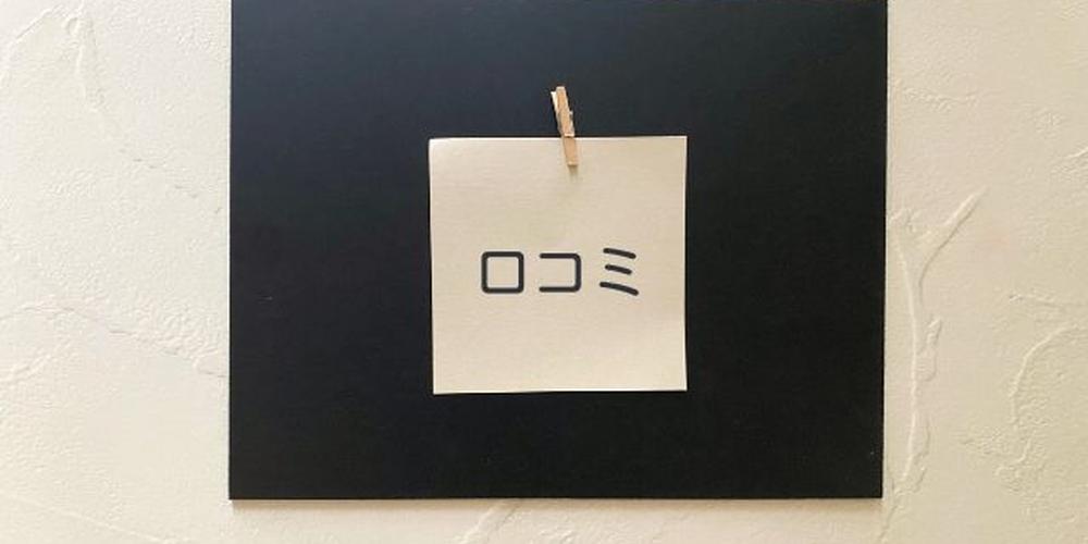 黒板に貼られた「口コミ」のメモとシンプルな壁背景のイメージ画