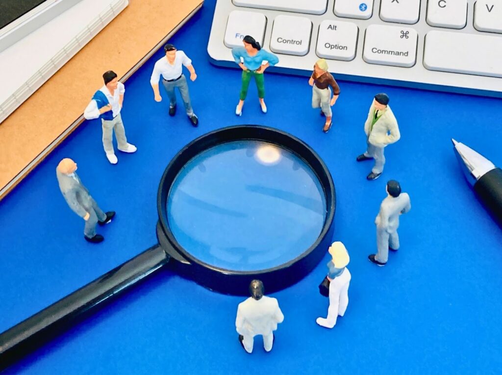 虫眼鏡を囲むように複数の人の模型が置かれている画像